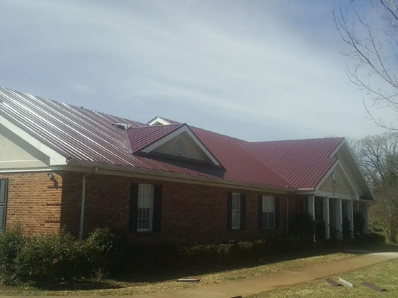 Red metal roof with gabled entries on a long brick building, from a Hail Damage Roof Repair job in Hoquiam