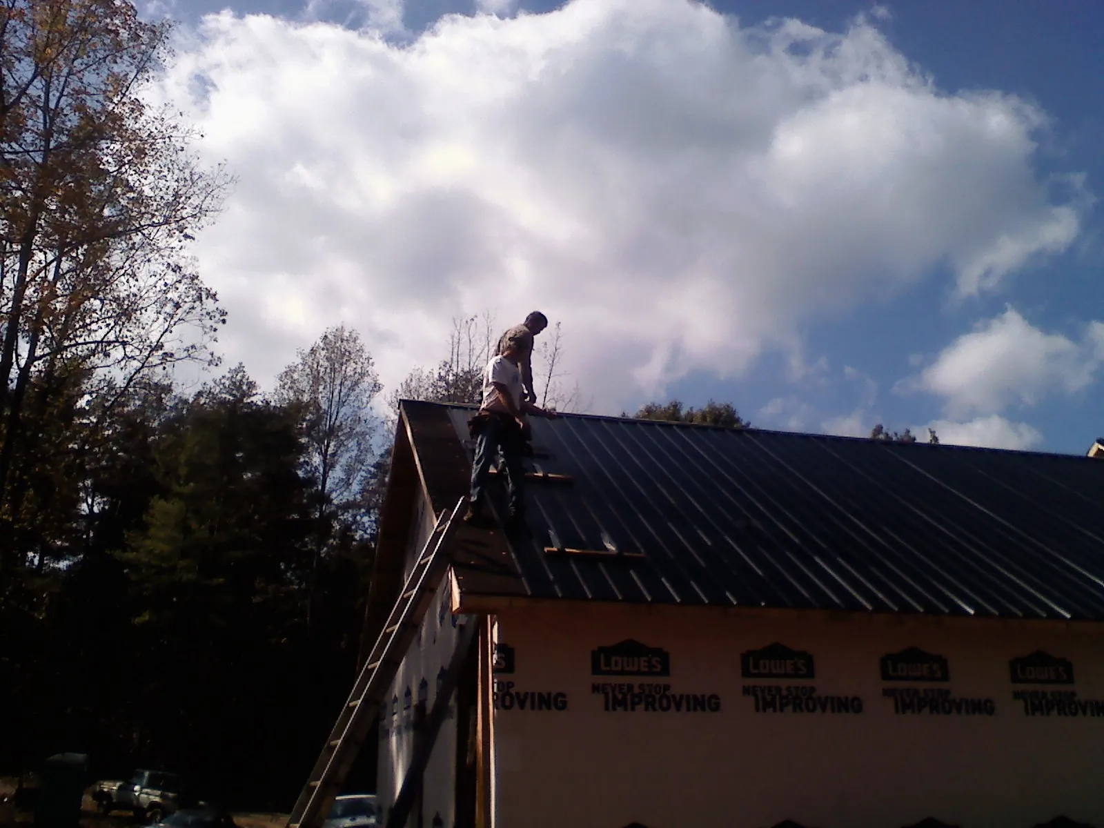 Roofer fastening dark metal panels high against a cloudy sky, from a Roof Inspection job in Hoquiam