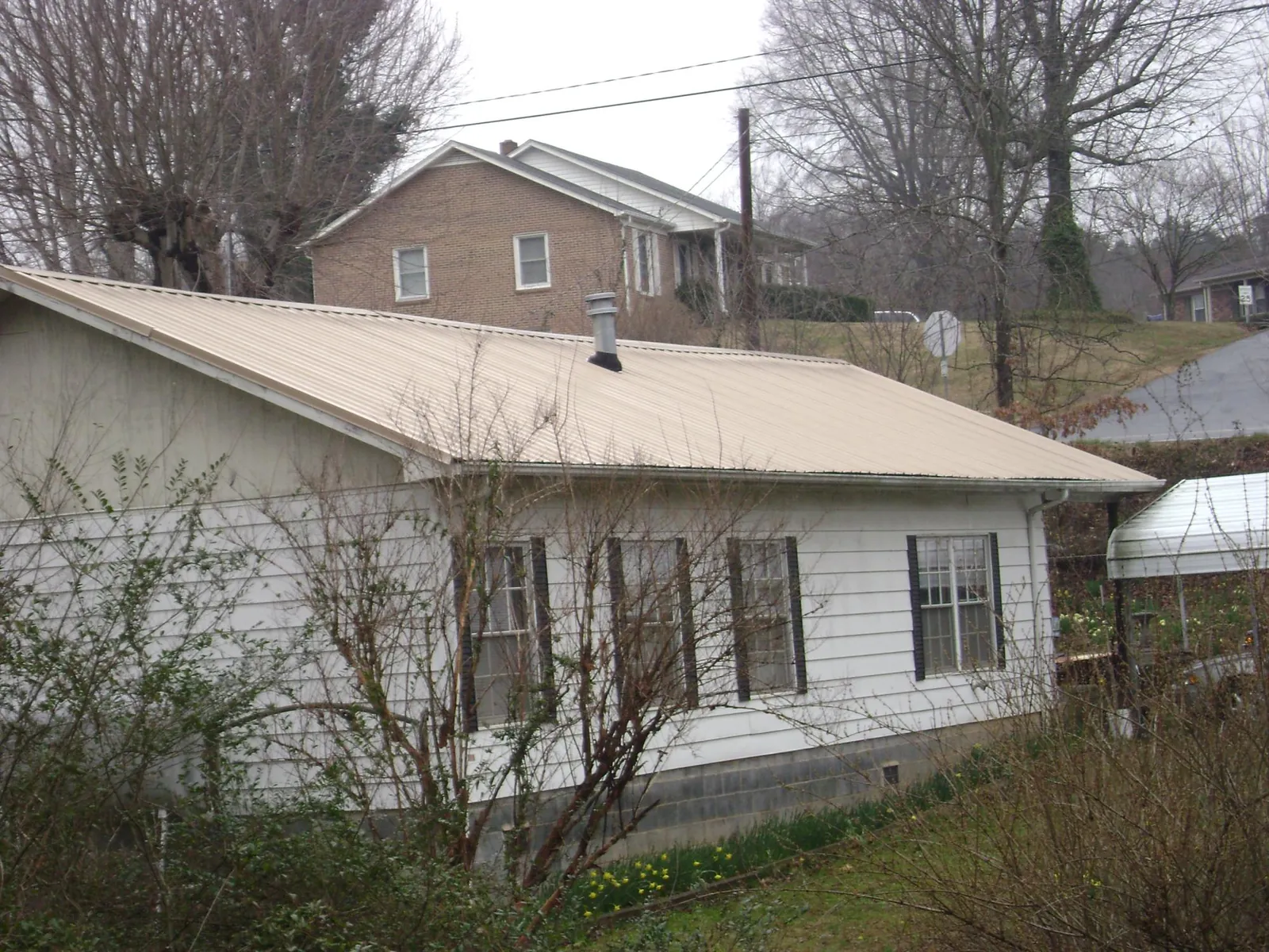 Tan metal roof on a white sided house set into a hillside — Commercial Roofing by Roofing Brothers in Hoquiam